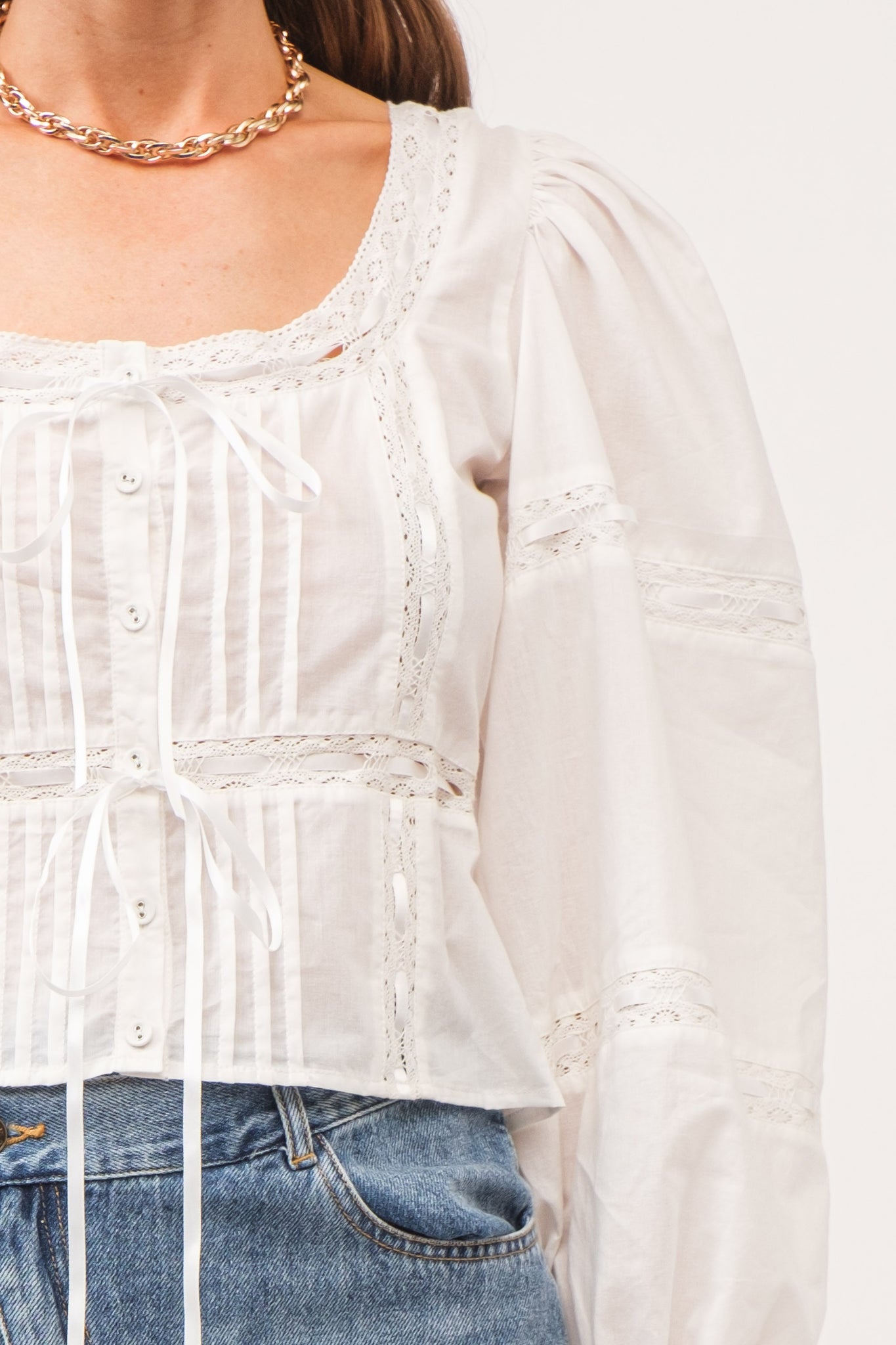 close up of blouse with pleating detailing and lace with white ribbon details